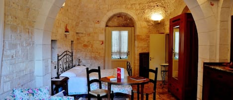A room with a stone wall, a bed, a floral sofa, a wooden table, and a chair.