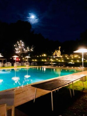 A nighttime swimming pool with lounge chairs and umbrellas, surrounded by trees and a statue. - Tenuta Monacelle (Monopoli)