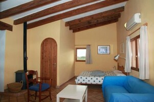 Una habitación acogedora con cama, un sofá azul, una puerta de madera, una mesita y una ventana con cortinas.