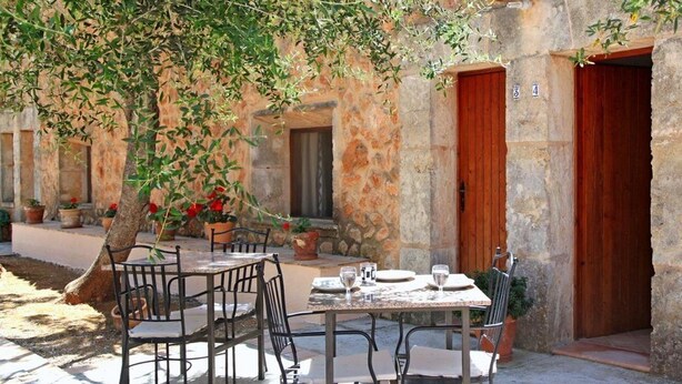 An outdoor dining area with stone walls, wooden doors, and potted plants. - Finca Son Guardiola (Llucmajor)