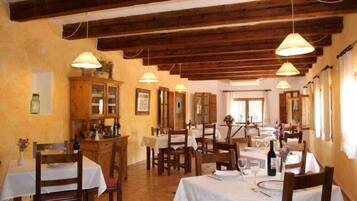 A restaurant with wooden beams, white tablecloths, and hanging lamps.