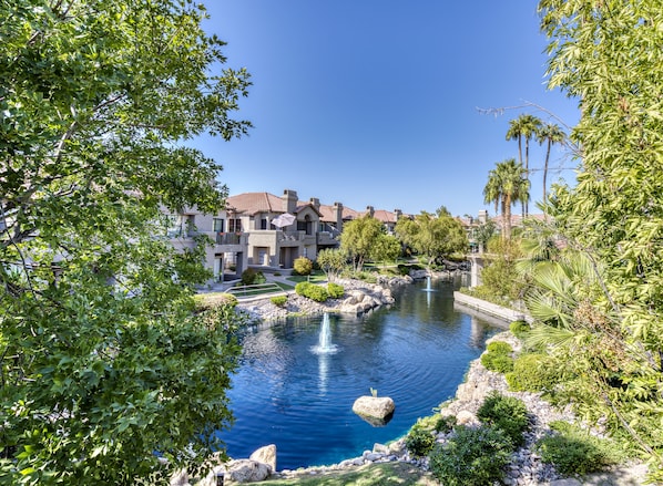 A resort with a central water feature, including a fountain, surrounded by lush greenery and palm trees.