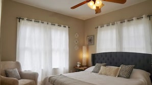 Quarto com uma cama grande, uma cadeira, um ventilador de teto e uma mesa de cabeceira com luminária.