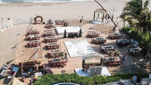 A beachside wedding setup with tables and chairs, a stage, and a pool. - Mishol Hotel And Beach Club (Acapulco)