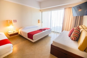 A hotel room with two beds, a TV, a window with curtains, and a bedside table with a lamp.