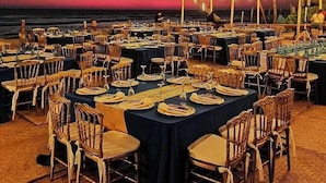 An outdoor dining area with tables and chairs arranged for a meal, overlooking the ocean at sunset. - Mishol Hotel And Beach Club (Acapulco)