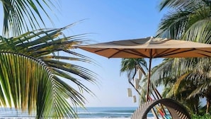 An outdoor seating area with tables and chairs, a large umbrella, and a view of the ocean. - Mishol Hotel And Beach Club (Acapulco)
