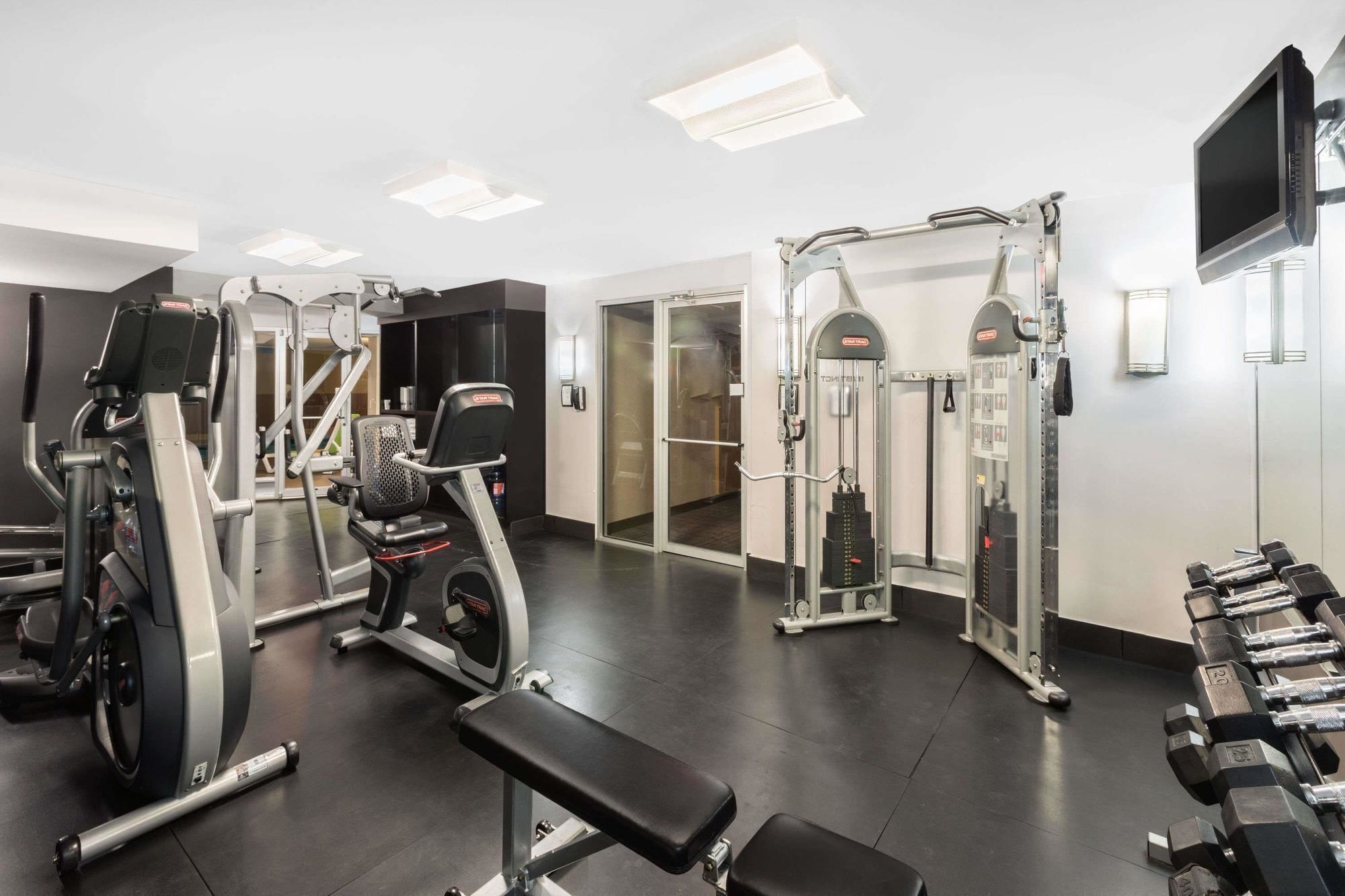 Un gimnasio con diferentes equipos de ejercicio, incluyendo una cinta de correr, máquinas de pesas y mancuernas.