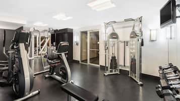 Un gimnasio con diferentes equipos de ejercicio, incluyendo una cinta de correr, máquinas de pesas y mancuernas.