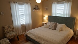 Een slaapkamer met een bed, een stoel, een nachtkastje en een lamp.