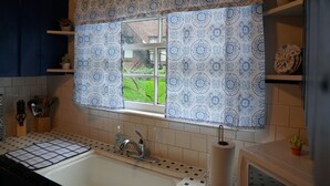 Een keuken met raambekleding met een patroon, een spoelbak en een raam met uitzicht op een groen gebied.