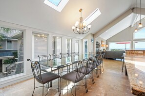 A spacious kitchen with a long dining table, modern chandelier, and large windows. - Stunning oceanfront home offering private pool & hot tub, steps from Coligny! (Hilton Head)