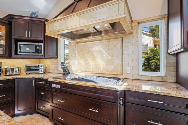 A kitchen with dark wood cabinets, a granite countertop, a stainless steel range hood, a microwave, and a toaster.