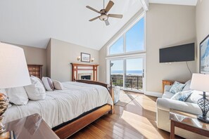A bedroom with a bed, a ceiling fan, a fireplace, a TV, and a balcony with a view. - Stunning oceanfront home offering private pool & hot tub, steps from Coligny! (Hilton Head)