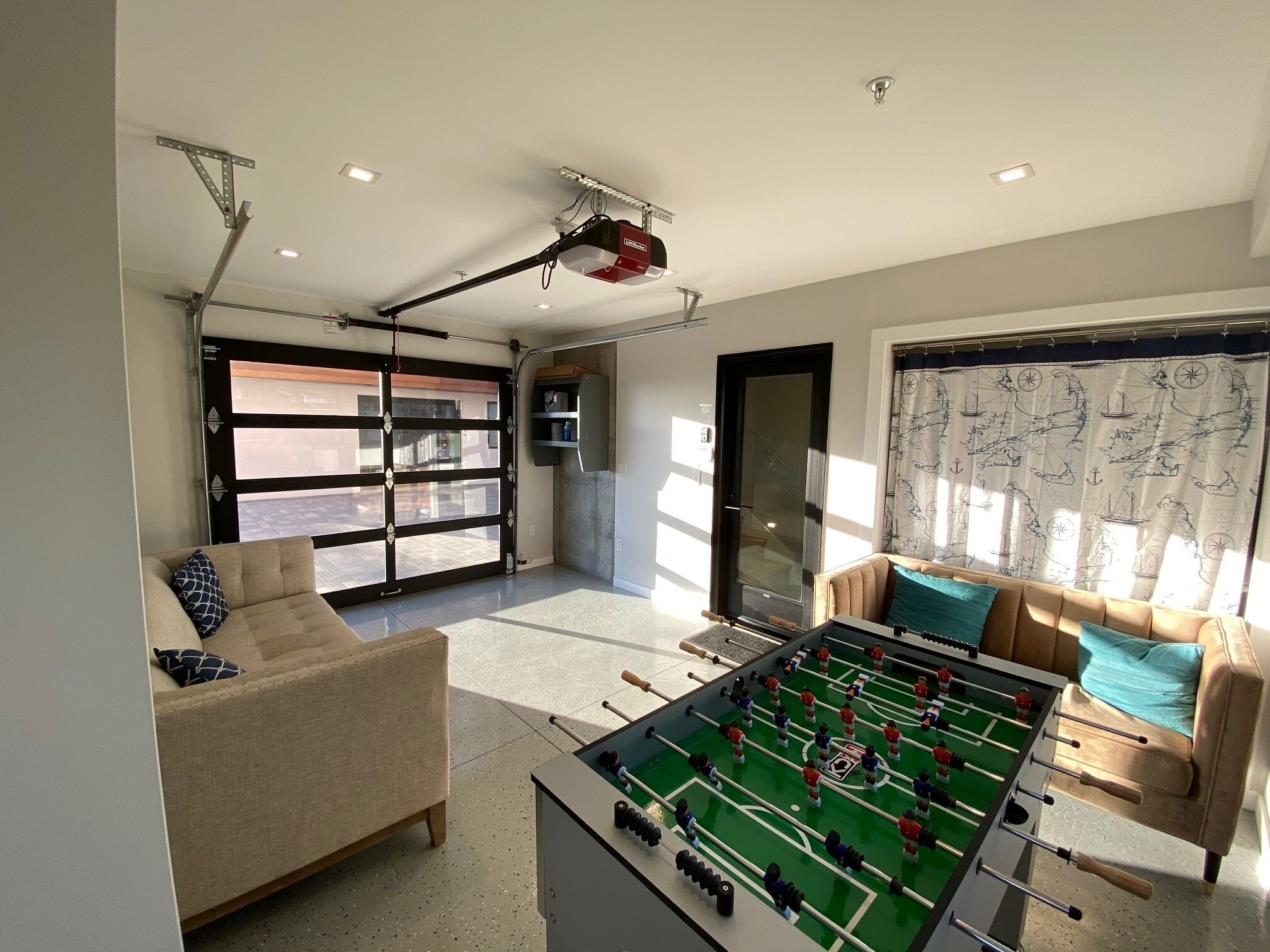 Amplia sala de estar con mesa de fútbol, un sofá y un gran ventanal corredizo que da a un patio exterior.