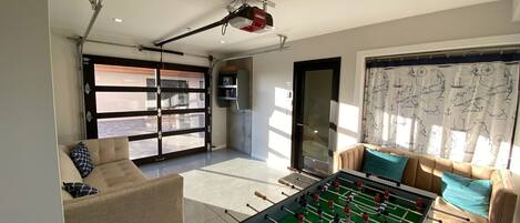 Amplia sala de estar con mesa de fútbol, un sofá y un gran ventanal corredizo que da a un patio exterior.