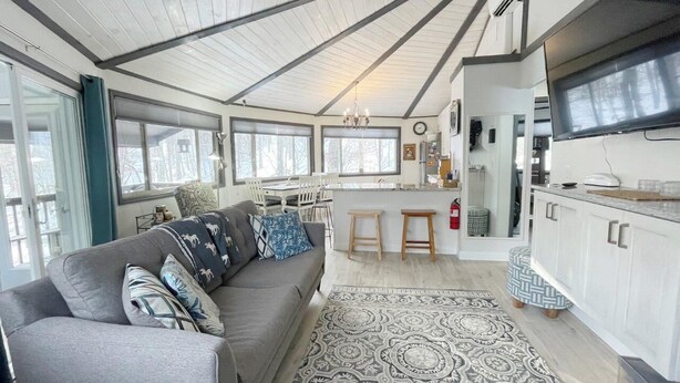 A spacious living area with a gray sofa, patterned rug, and a kitchen with white cabinets and a large TV. - Summer is here, cool down on Beech mountain! (Beech Mountain)