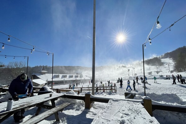A snowy outdoor area with picnic tables and a ski slope in the background. - Summer is here, cool down on Beech mountain! (Beech Mountain)