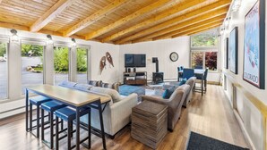 A spacious living area with a wooden ceiling, a television, and a fireplace. There are multiple seating options including sofas and a dining table.