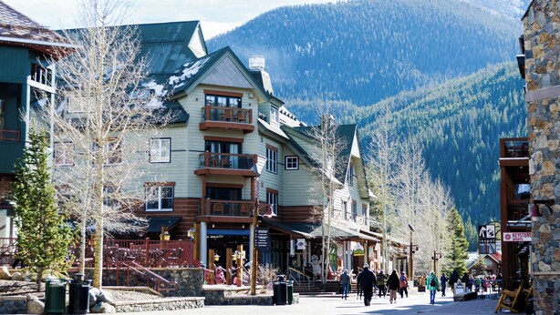 A multi-story building with a balcony, a stone facade, and a mountainous backdrop.