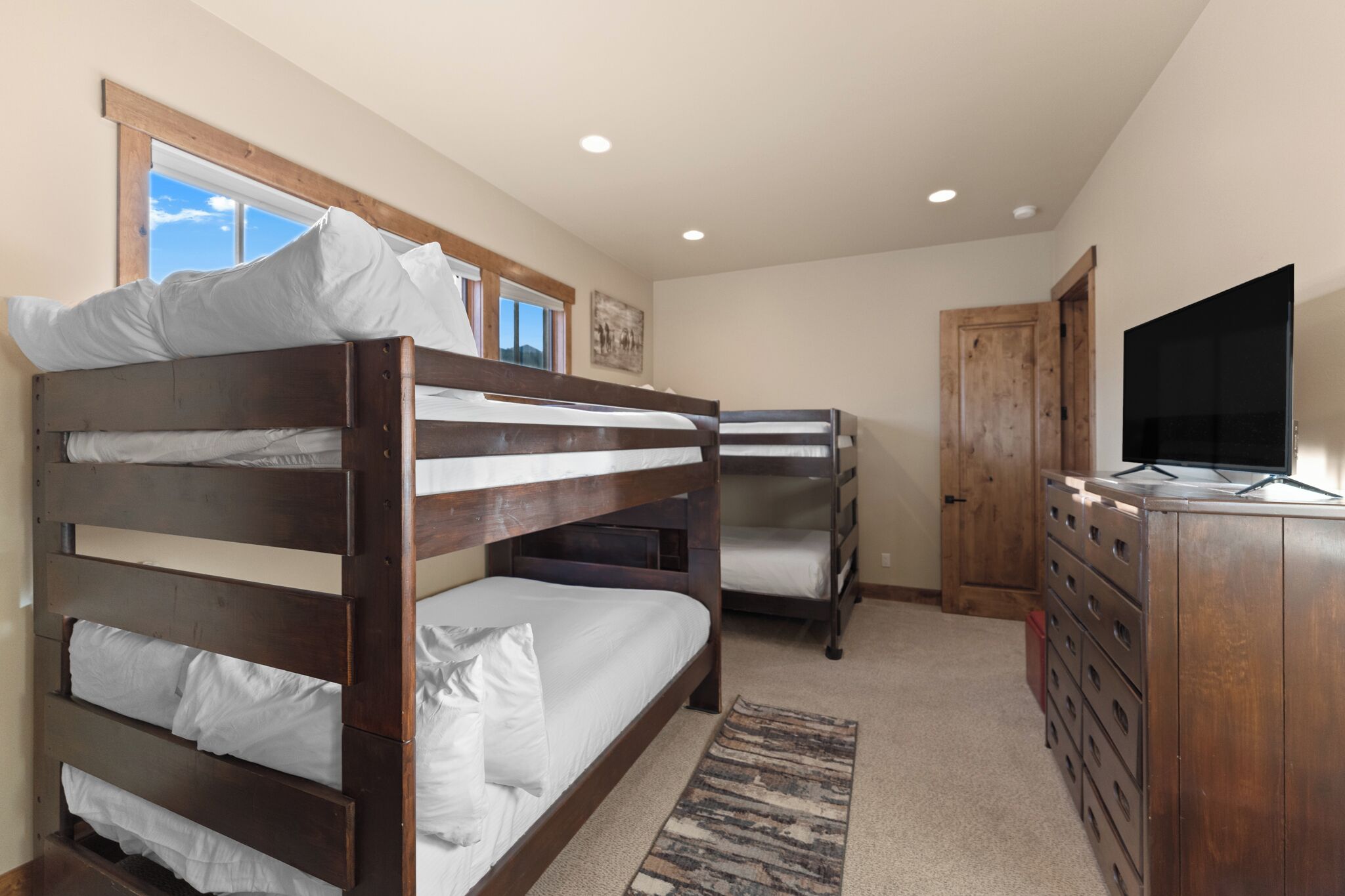 A bedroom with bunk beds, a dresser, a television, and a window with a view.