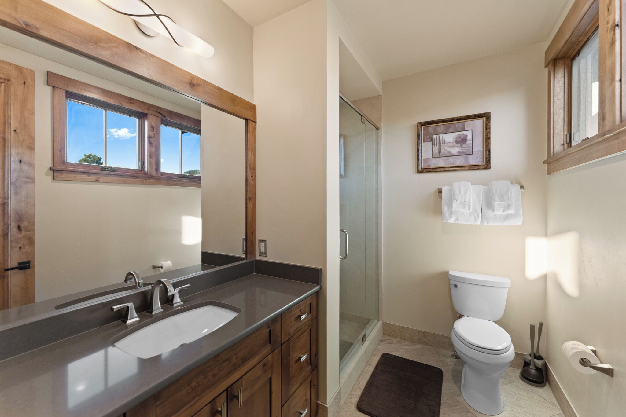 A bathroom with a wooden vanity, a large mirror, a shower, and a toilet.