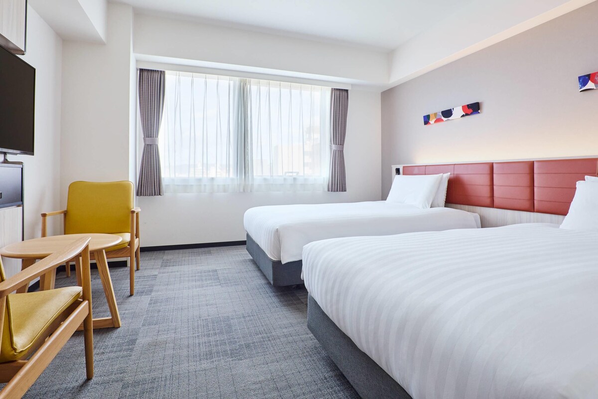 Ett hotellrum med två sängar, ett skrivbord, en stol och en TV.