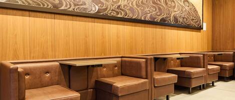 Une rangée de banquettes en cuir marron avec des tables, des panneaux de bois sur les murs et une grande fresque murale abstraite.