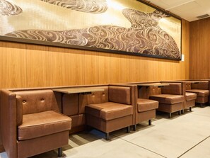 Filas de cabinas de cuero marrón con mesas, paneles de madera en las paredes y un gran mural abstracto.