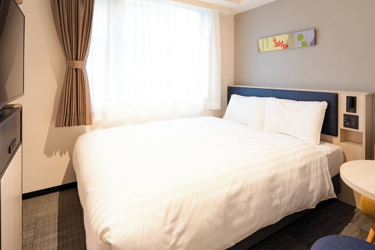 A hotel room with a bed, a desk, a chair, a TV, and a wall-mounted artwork.