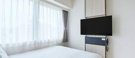 A hotel room with a large bed, a flat-screen TV mounted on the wall, and a window with sheer curtains.