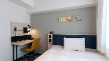 A hotel room with a bed, a desk with a chair, a wall-mounted TV, and a small shelf.