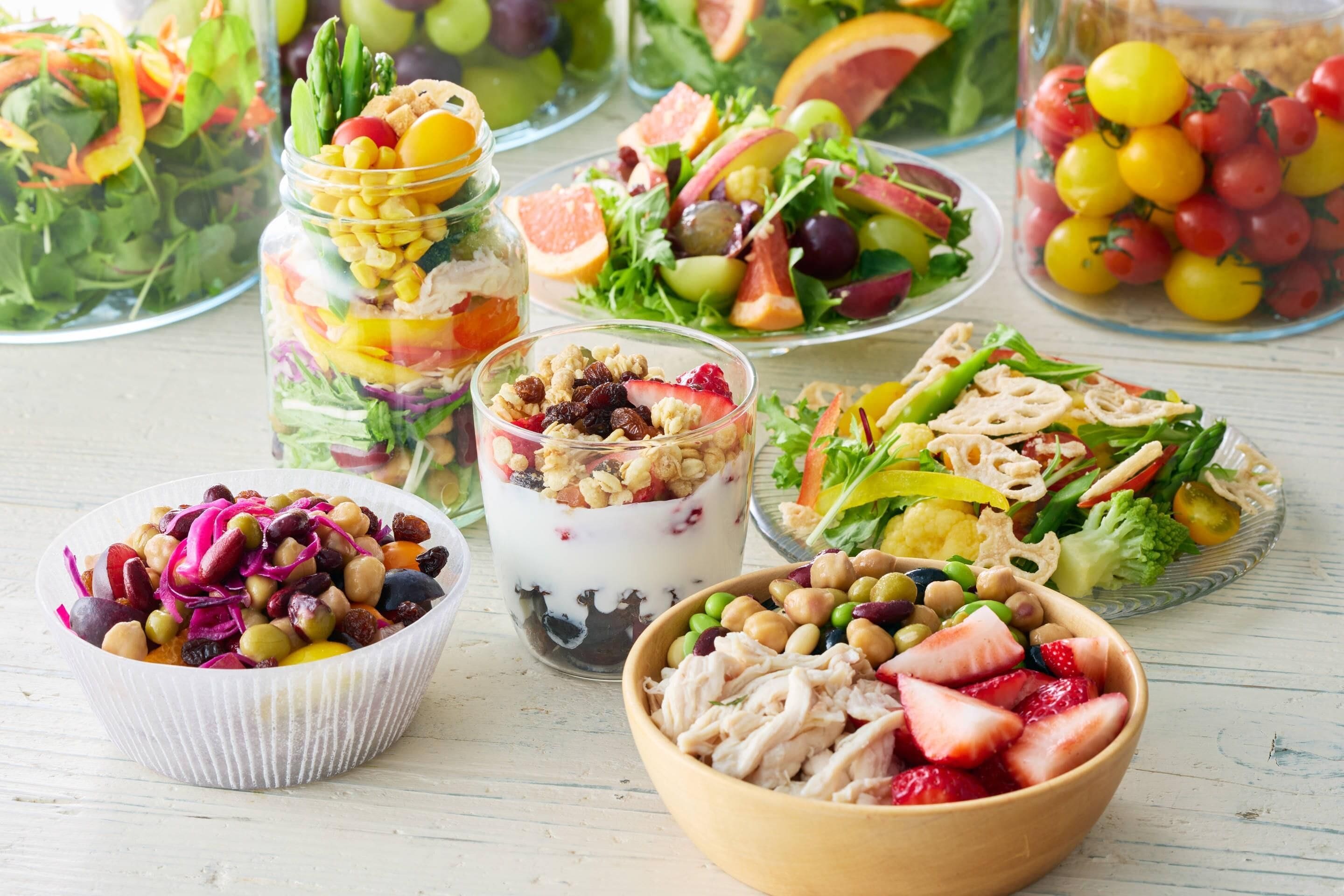 Diversos platos de comida, incluyendo ensaladas, un tazón de pollo con fresas y un parfait de yogur.