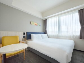 Habitación de hotel con cama, una silla, una mesita, televisor montado en la pared y una ventana con cortinas.