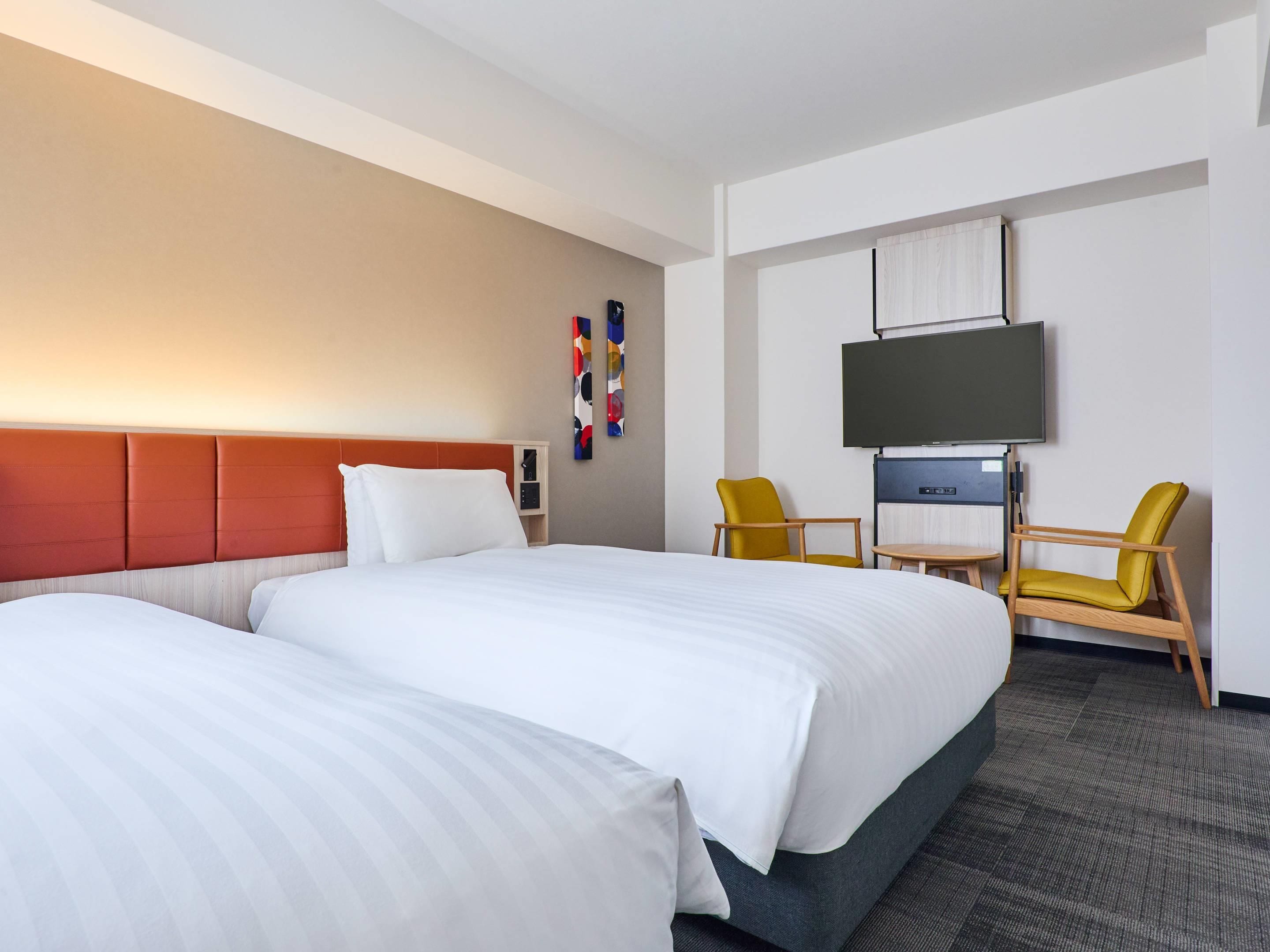 Habitación de hotel con dos camas, un televisor, una mesita y dos sillas.