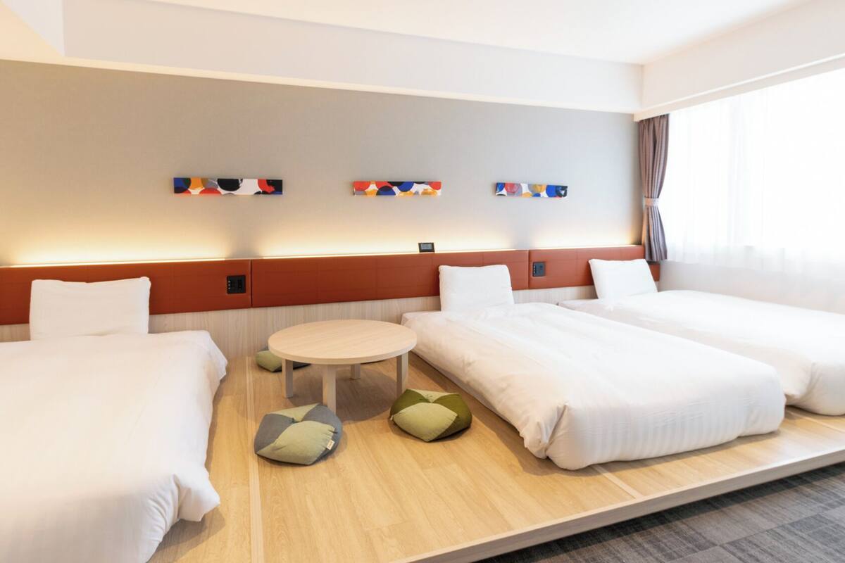 A hotel room with two beds, a small round table, and a wall-mounted control panel.