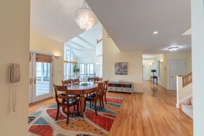 Uma sala de jantar ampla, com uma mesa e cadeiras de madeira, um tapete colorido e um candelabro.