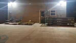 Een gebouw met een houten gevel, een deur en twee ramen. Buiten staan twee lounge fauteuils en een bank.