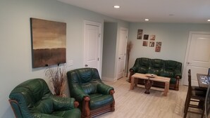 Een woonkamer met twee groene leren fauteuils, een houten salontafel en een groene bank.