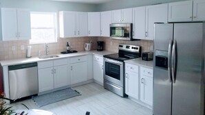 Een moderne keuken met witte kastjes, roestvrijstalen apparatuur en een raam dat voor natuurlijk licht zorgt.