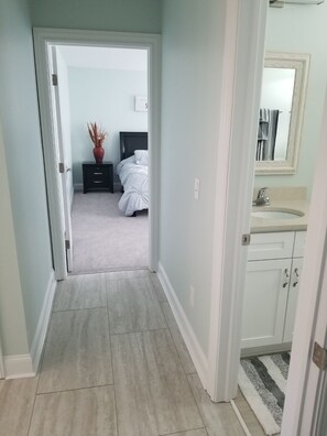 Un couloir étroit mène à une chambre à coucher qui contient un lit, une table de chevet et un vase rempli de plantes séchées.