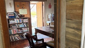 Un intérieur rustique avec un plancher en bois, une bibliothèque remplie de livres, une table à manger avec des chaises et un ventilateur de plafond.