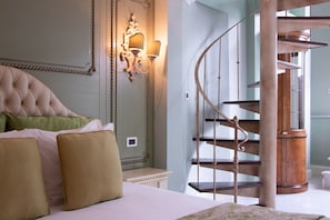 A bedroom with a tufted headboard, a wooden spiral staircase, and a wall-mounted light fixture. - Villa Palma Boutique Hotel (Panama City)