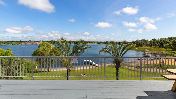 A deck with a view of a lake, palm trees, and a warning sign.