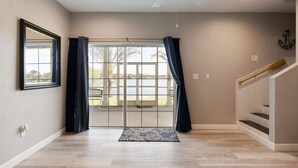 A spacious room with a large sliding glass door leading to a balcony, a ceiling fan, and a wooden staircase.