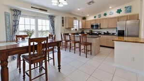 A kitchen with wooden cabinets, a central island, and a dining area with wooden chairs.