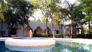 A courtyard with a circular pool, palm trees, and a building with arches. - Full Hacienda Santuario Noc Ac (Mérida)