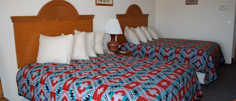 Habitación de hotel con dos camas, cada una con ropa de cama estampada, cabeceros de madera, una lámpara de noche y una mesita.