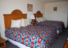 Habitación de hotel con dos camas, cada una con ropa de cama estampada, cabeceros de madera, una lámpara de noche y una mesita.