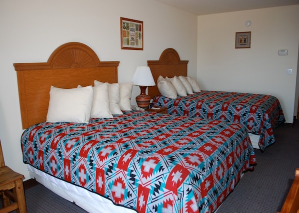 Ein Hotelzimmer mit zwei Betten, jeweils mit gemusterten Bettbezügen, einem Holzkopfstück, einer Nachttischlampe und einem kleinen Tisch.
